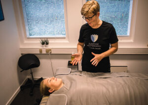 Behandling med infrarød varme hos Susanne Vestergaard, hvor en kunde ligger under en varmetæppe, mens behandleren forklarer proceduren.
