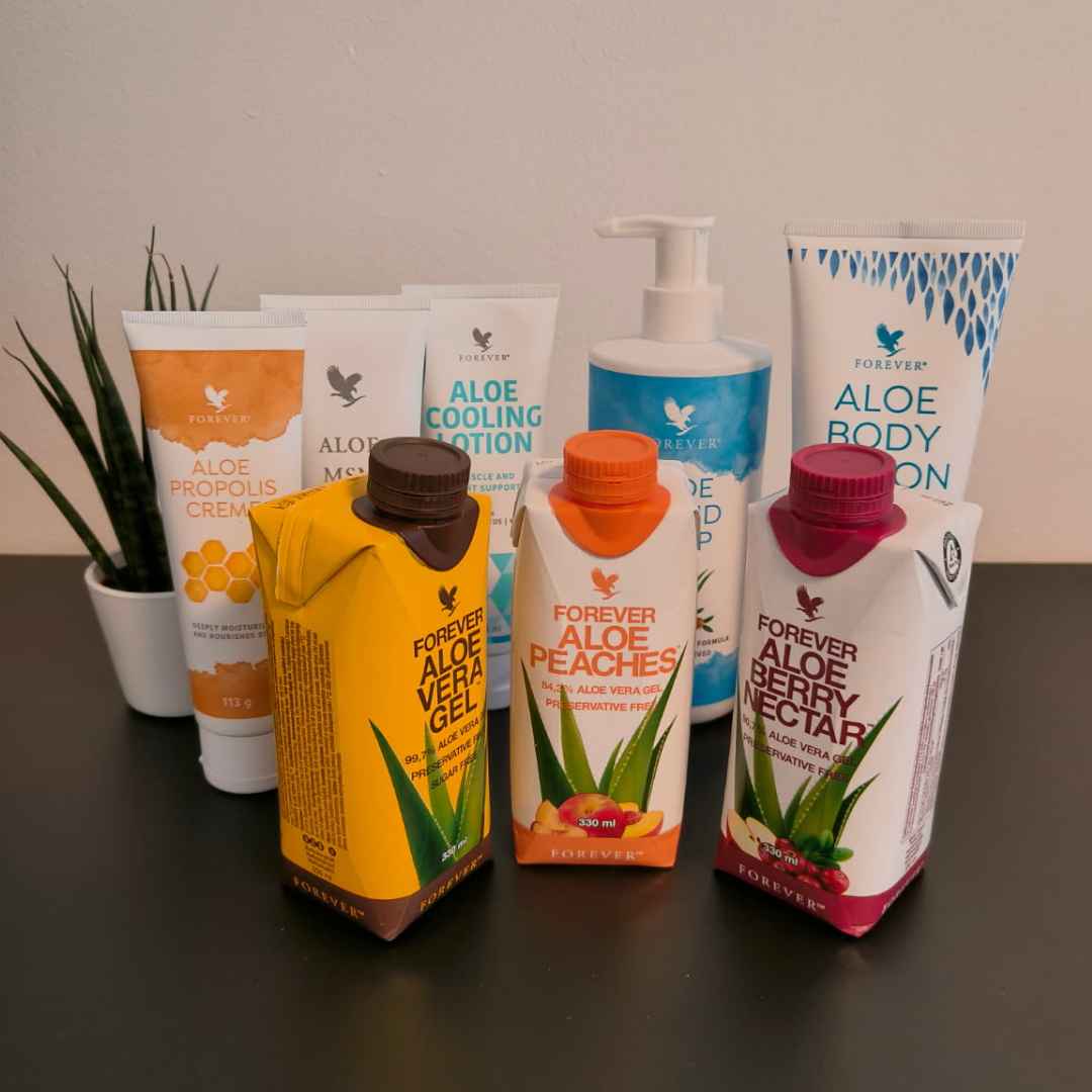 Susanne Vestergaard (1) Et udvalg af Forever Living aloe vera produkter, herunder drikke og hudpleje, stillet op på et bord med en lille plante i baggrunden.