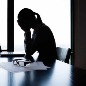 Kvinde sidder ved et skrivebord med hænderne mod ansigtet, tydeligt påvirket af senfølger af stress.