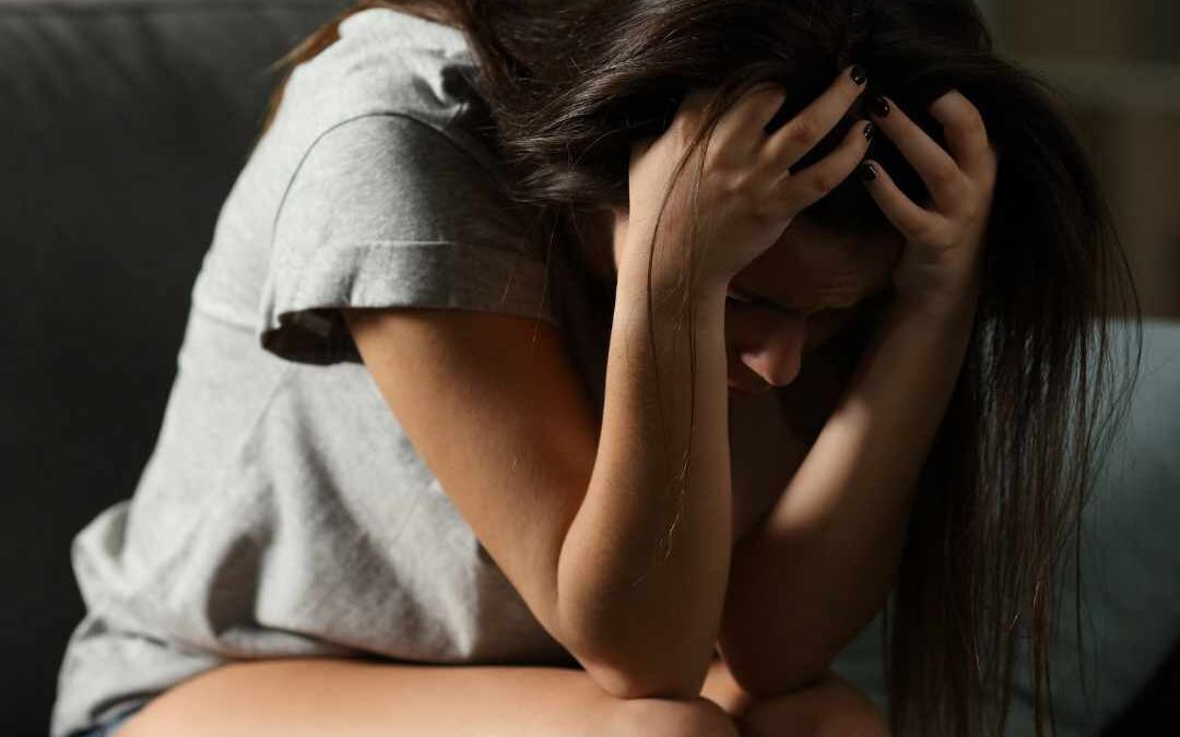 Kvinde sidder på sofaen med hænderne i håret og hovedet bøjet, tydeligt påvirket af uro og stress.