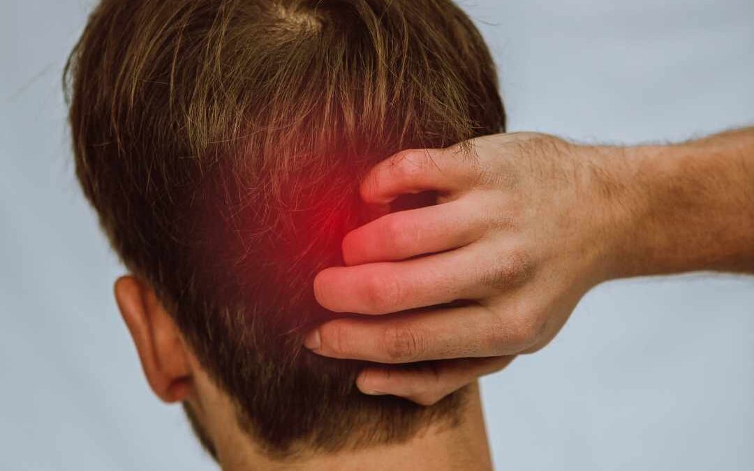 Mand med hovedpine i baghovedet holder sig på nakken med smerteudstråling fra bagsiden af hovedet.