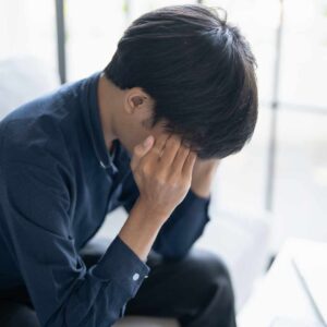 Mand med hovedpine i panden sidder med hænderne mod tindingerne og hovedet bøjet forover i smerte.