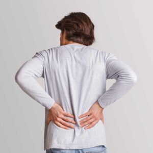 Mand i grå bluse set bagfra holder sig på lænden med begge hænder – illustrerer smerter i muskler og led.