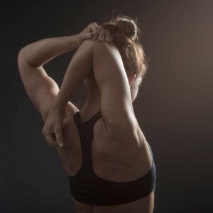 Kvinde i sort sportstop laver udstrækningsøvelse for skulder og overarm – fokus på fleksibilitet og smidighed.
