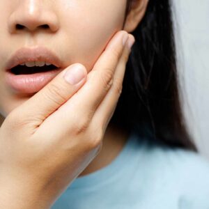 Kvinde holder sig på kæben med smertefuldt udtryk og let åben mund, hvilket indikerer kæbespændinger eller ubehag i kæbeområdet.