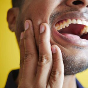Mand holder sig på kinden med synlig smerte og åben mund, hvilket indikerer spændinger i kæben.