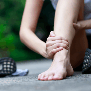 Person holder om sin ankel og forfod med begge hænder – indikerer smerter i forfod og tæer, muligvis efter fysisk aktivitet.