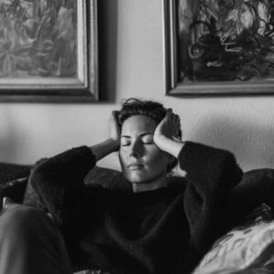 Kvinde med lukkede øjne og hænder mod hovedet som et udtryk for behovet for behandling af tankemylder og indre uro.