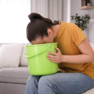 Kvinde med kvalme og svimmelhed, der sidder klar til at kaste op i spand.