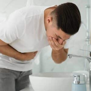 Mand med hånden for munden og smerter i maven, som oplever svimmelhed og kvalme.