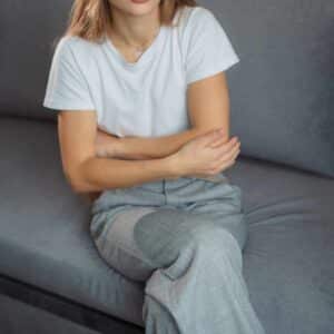 Kvinde sidder på sofa og holder sig om maven med tydeligt ubehag i kroppen, som kan skyldes stress, angst eller spændinger.