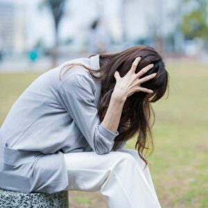 Kvinde sidder foroverbøjet og holder sig til hovedet med tegn på angst, stress eller uro – illustration af behov for angst behandling.