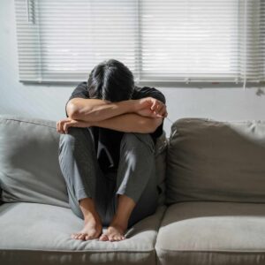 Mand sidder sammenkrøbet på sofa med hovedet begravet i armene, viser tegn på angst og behov for professionel angst behandling.