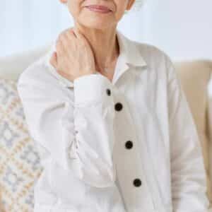 Ældre kvinde rører ved sin nakke med et udtryk af ubehag i kroppen, hvilket kan skyldes spændinger eller smerter.