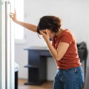 Kvinde med hånden for panden og tydelige tegn på svimmelhed og utilpashed.