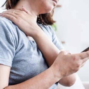 Kvinde med stive led i nakke og skuldre forårsaget af spændinger og stillesiddende arbejde.