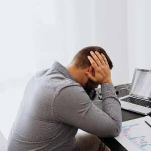 Mand ved skrivebord oplever nakkesmerter og hovedpine relateret til stillesiddende arbejde.