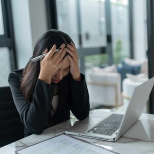 Kvinde sidder ved computer og holder sig til hovedet som tegn på stress symptomer hos kvinder.