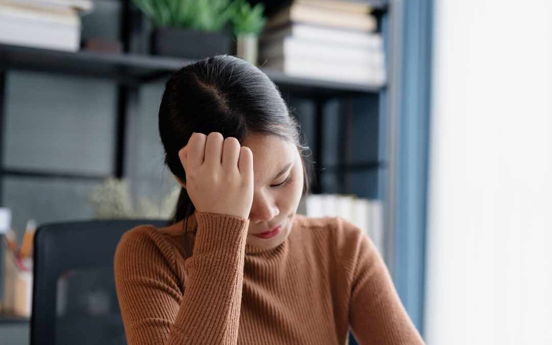 Kvinde sidder ved skrivebord og holder sig til hovedet med stresssymptomer.