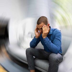 Mand oplever kraftig svimmelhed og ubehag siddende med hænderne mod hovedet som symptom på balanceproblemer.