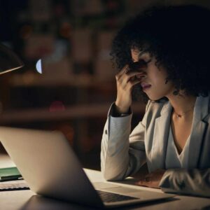 Kvinde ved computer holder sig til panden og viser tegn på udmattelse, stress og manglende energi.