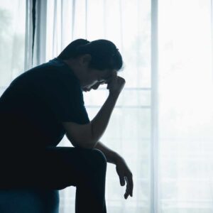 Person sidder alene med hovedet bøjet og virker udmattet som tegn på mental overbelastning og stress.